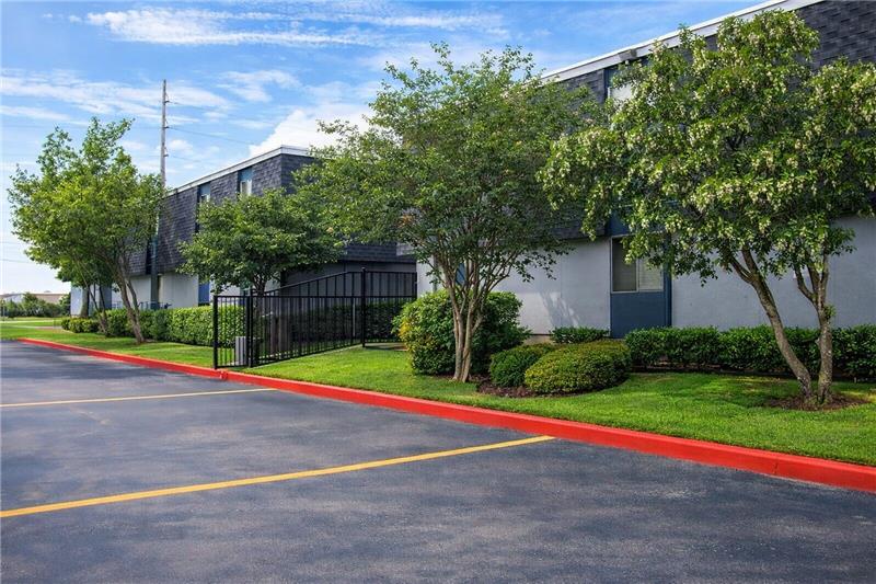 A parking lot in front of a building with a black fence and green trees.